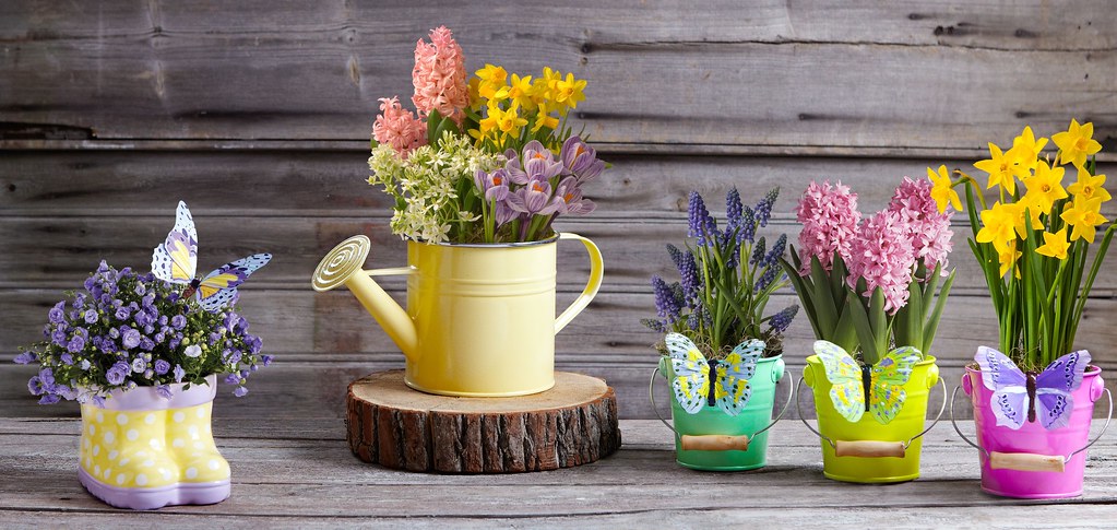 Yellow watering can used as a flower planter beside small pails of flowers