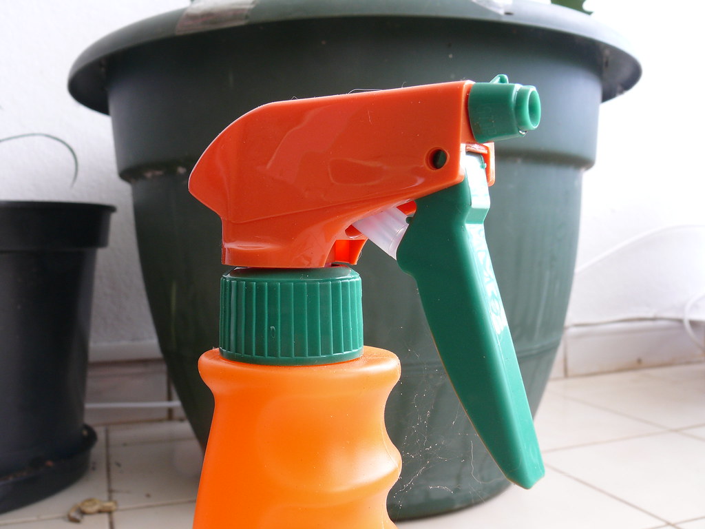 Orange and green spray bottle standing beside empty plant pots