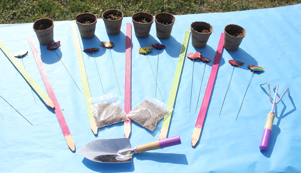 Small paper pots with colorful plant labels and garden tools on a blue table