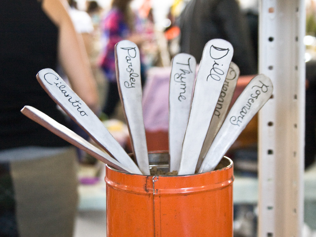 White herb plant markers with handwritten names in an orange container