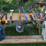 Garden tools, watering can, and hose reel spread across a wooden bench