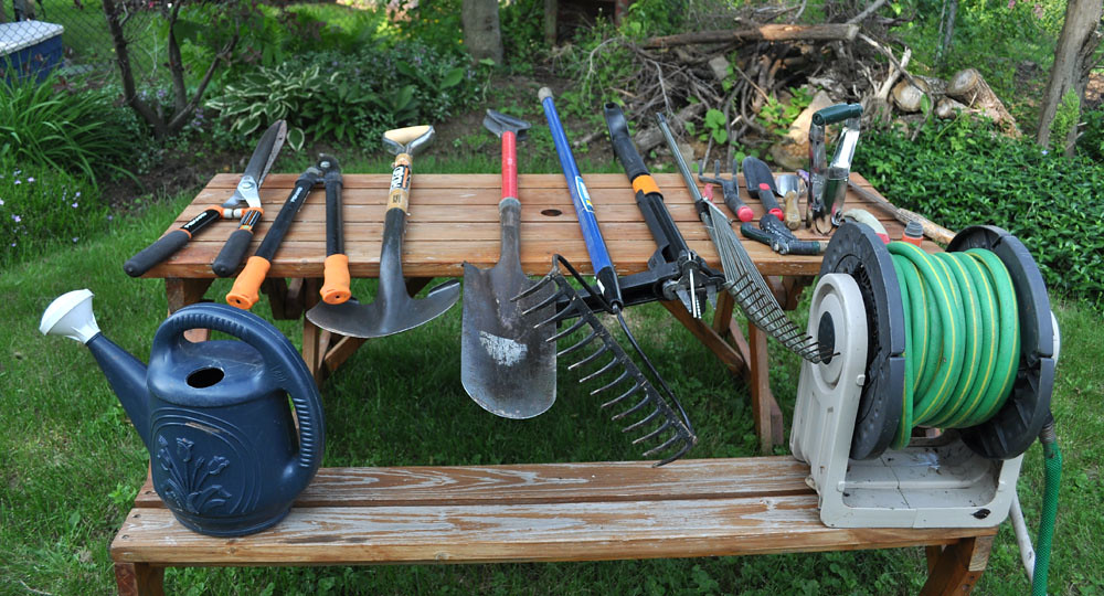 Garden tools, watering can, and hose reel spread across a wooden bench