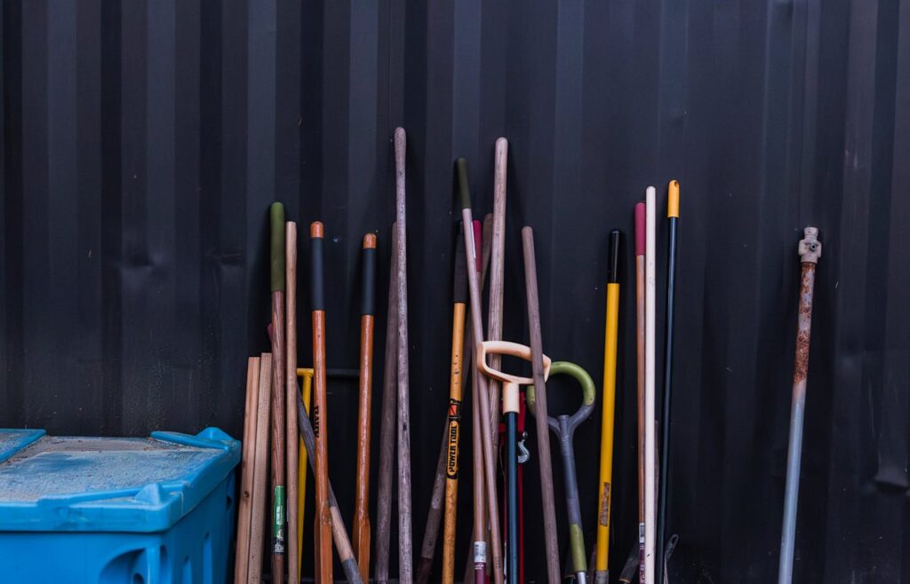 Long handled garden tools leaning against a dark wall