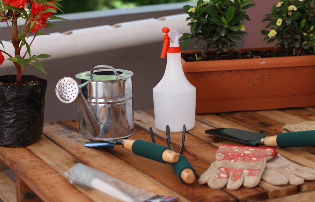 Watering can spray bottle gloves and garden hand tools on a wooden table